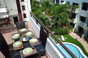 A balcony with a dining table set for four, overlooking a swimming pool and lush greenery.