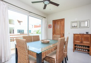 A dining area with a glass-top table, wicker chairs, a ceiling fan, and a wooden cabinet with a wine rack.
