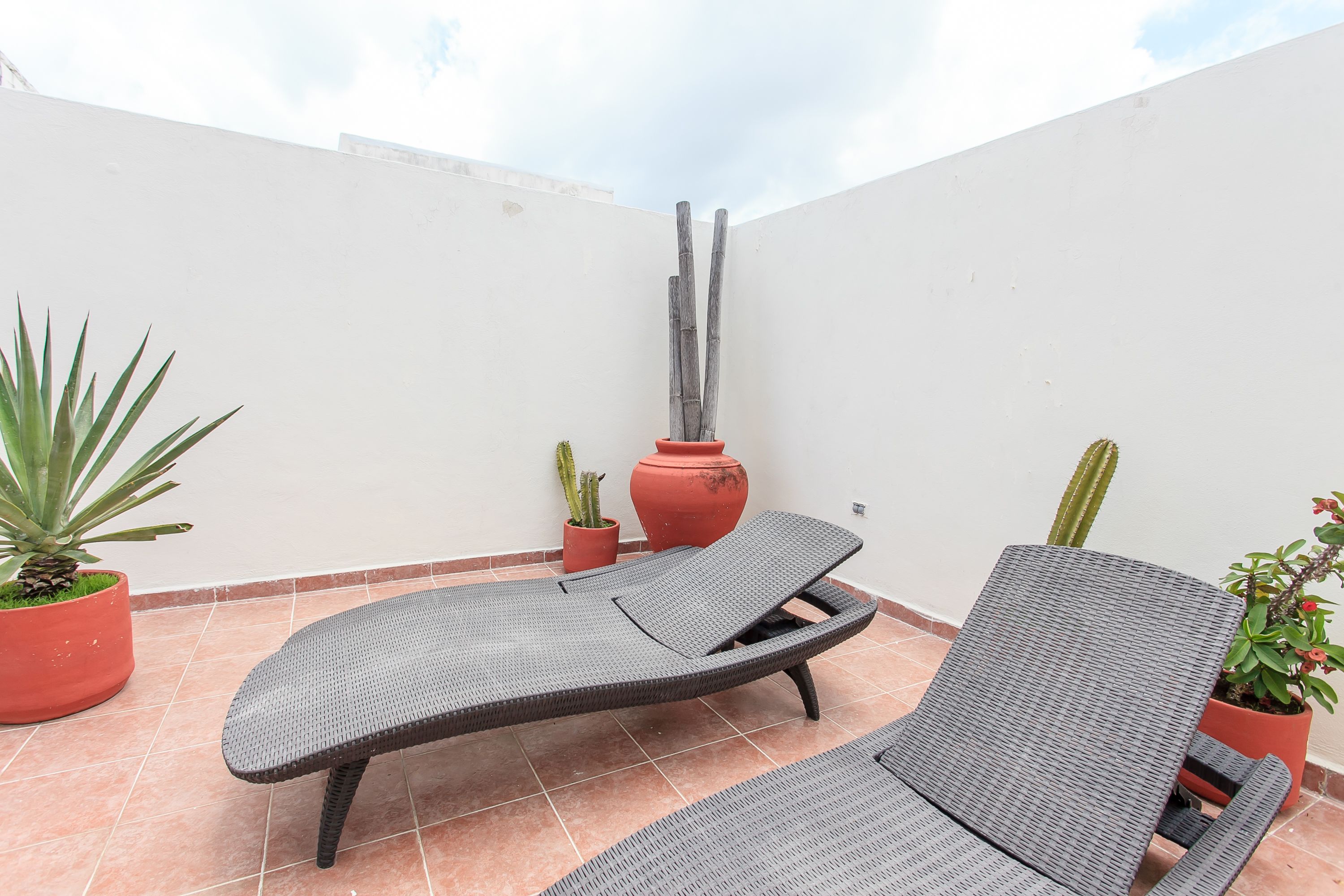 Una terraza en la azotea con dos sillones de descanso, plantas en macetas y una escultura alta.