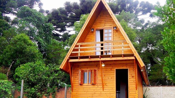 Uma cabana de madeira com telhado triangular, porta da frente e um pequeno alpendre.