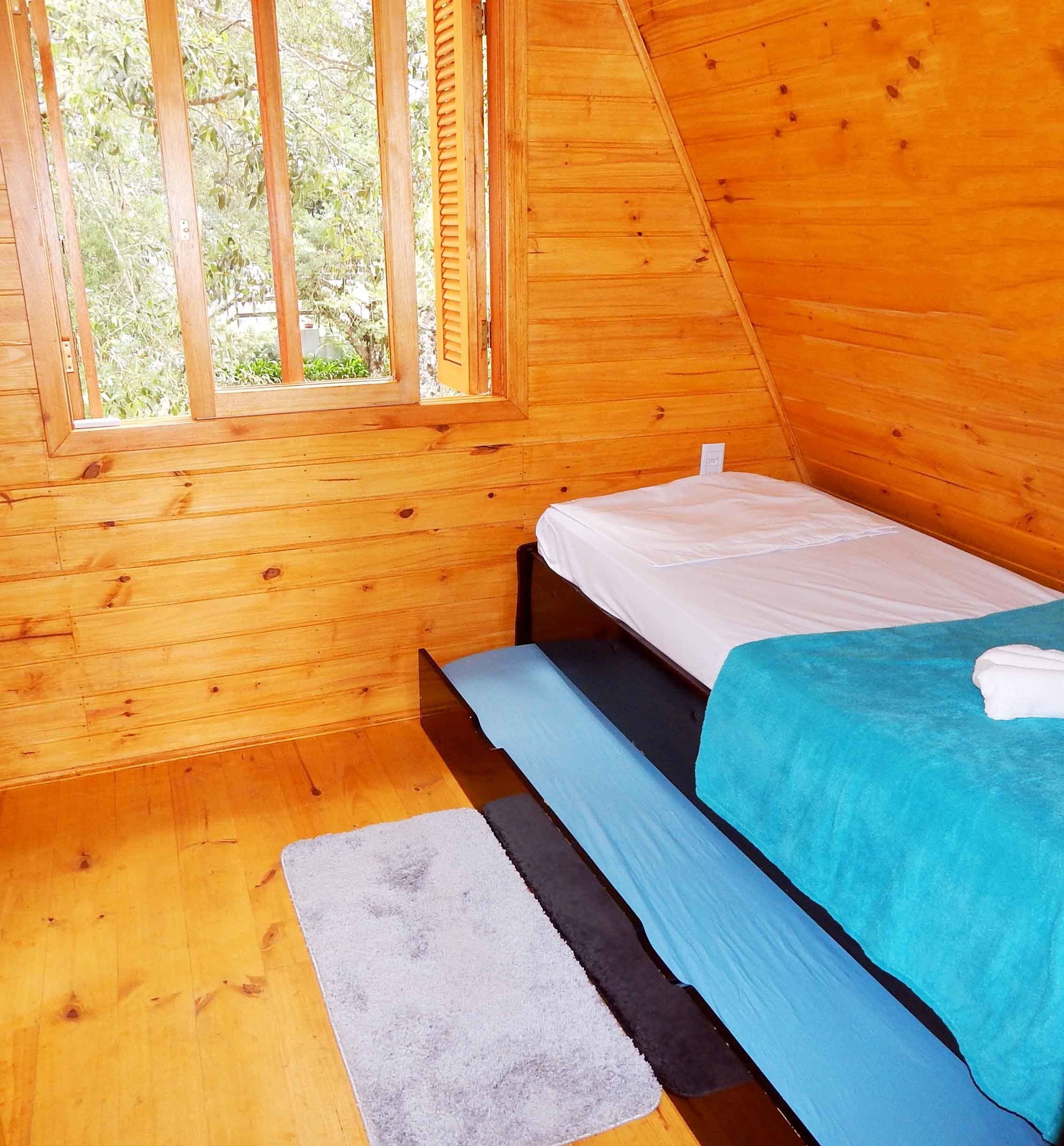 A small, wooden cabin bedroom with a single bed, a window, and a wooden floor.