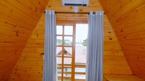 Quarto com painéis de madeira, uma cama, uma janela com cortinas e um aparelho de ar condicionado.