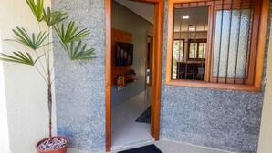 A doorway leading to a room with a tiled floor, a potted plant, and a window with bars. - Residencial de Luxe Ouro 01 (Canela)