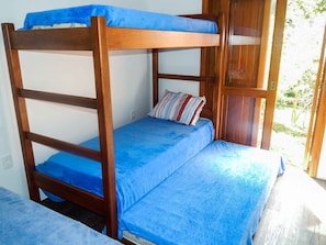 A bunk bed with a blue mattress and striped pillow, wooden frame, and a window with a view of greenery. - Residencial de Luxe Ouro 01 (Canela)