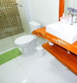A bathroom with a white toilet, a sink with a mirror, and a shower area. - Residencial de Luxe Ouro 01 (Canela)