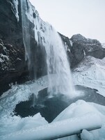 Una cascada vertiéndose en un estanque parcialmente congelado, rodeado de terreno nevado.