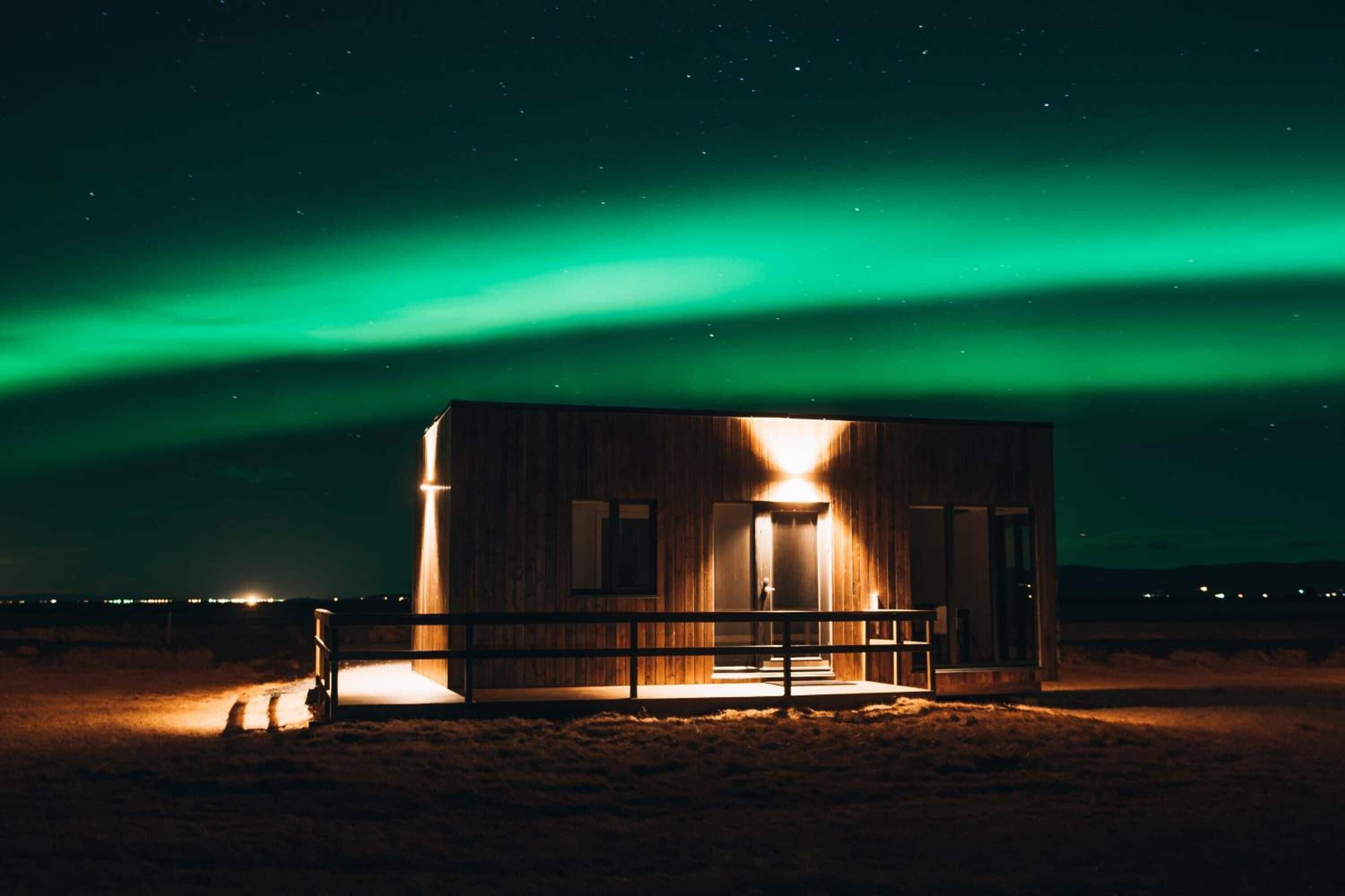 Una cabaña de madera con un porche, bajo un cielo nocturno con aurora boreal verde.
