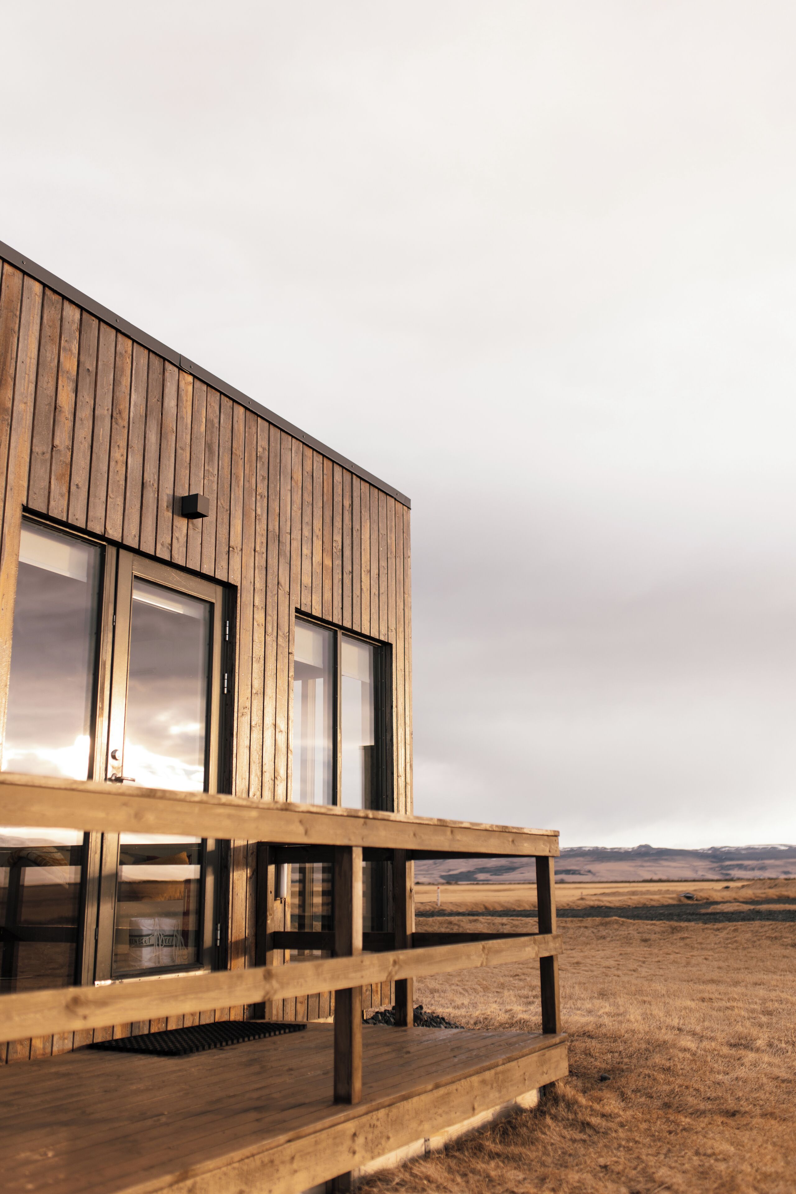 A wooden cabin with a deck, large windows, and a view of the landscape.