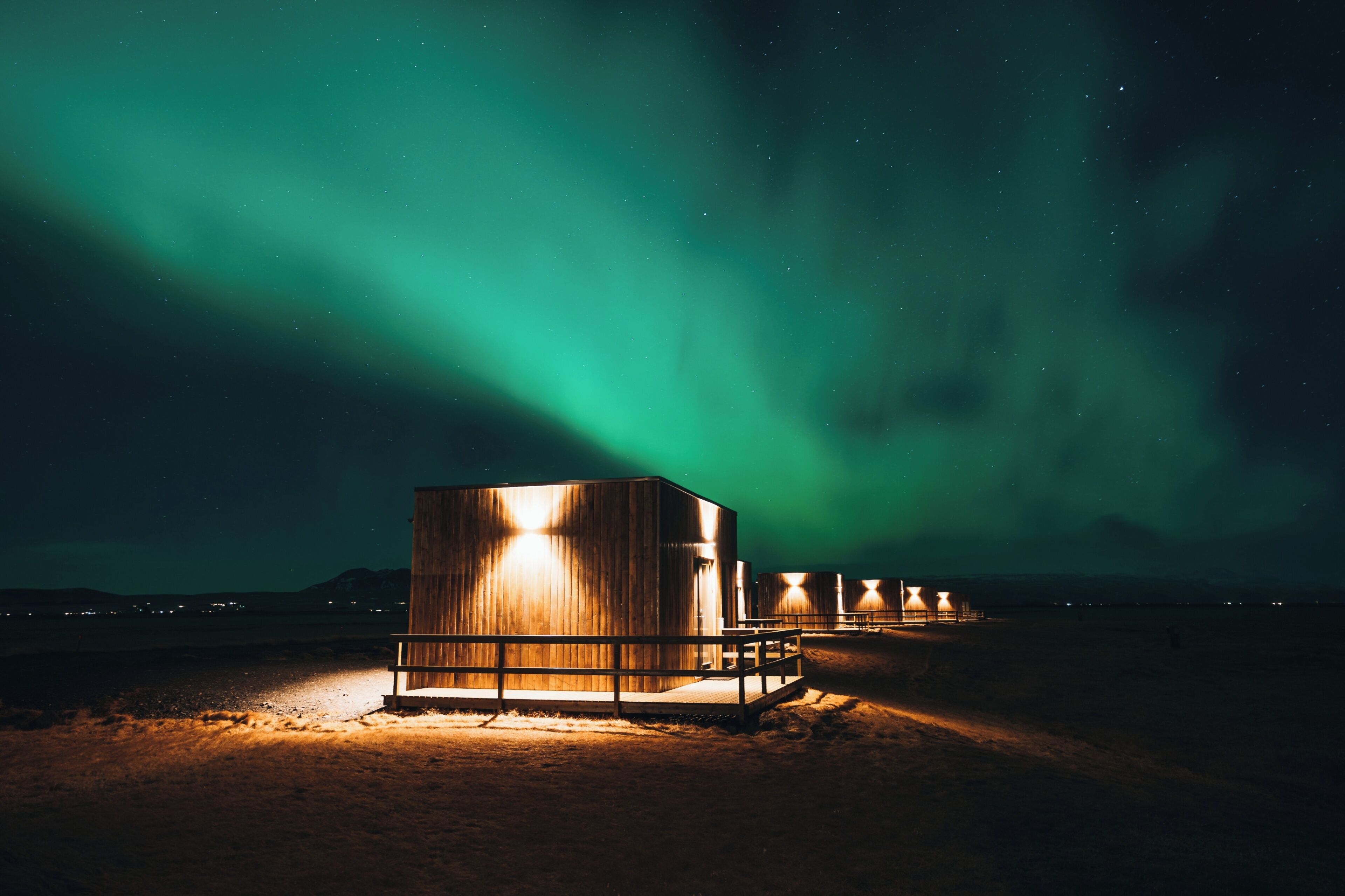 Une série de cabanes en bois aux fenêtres illuminées, se dressant sur fond d’aurores boréales.