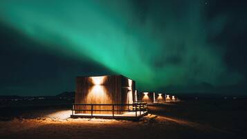 Une série de cabanes en bois aux fenêtres illuminées, se dressant sur fond d’aurores boréales.