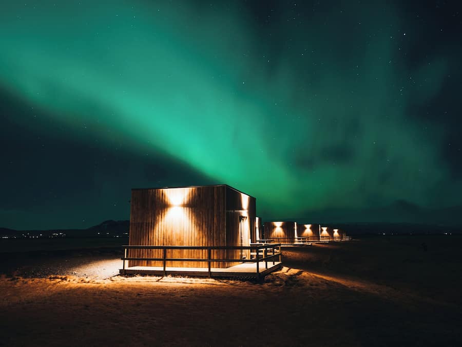 A series of wooden cabins with illuminated windows, set against a backdrop of the Northern Lights.