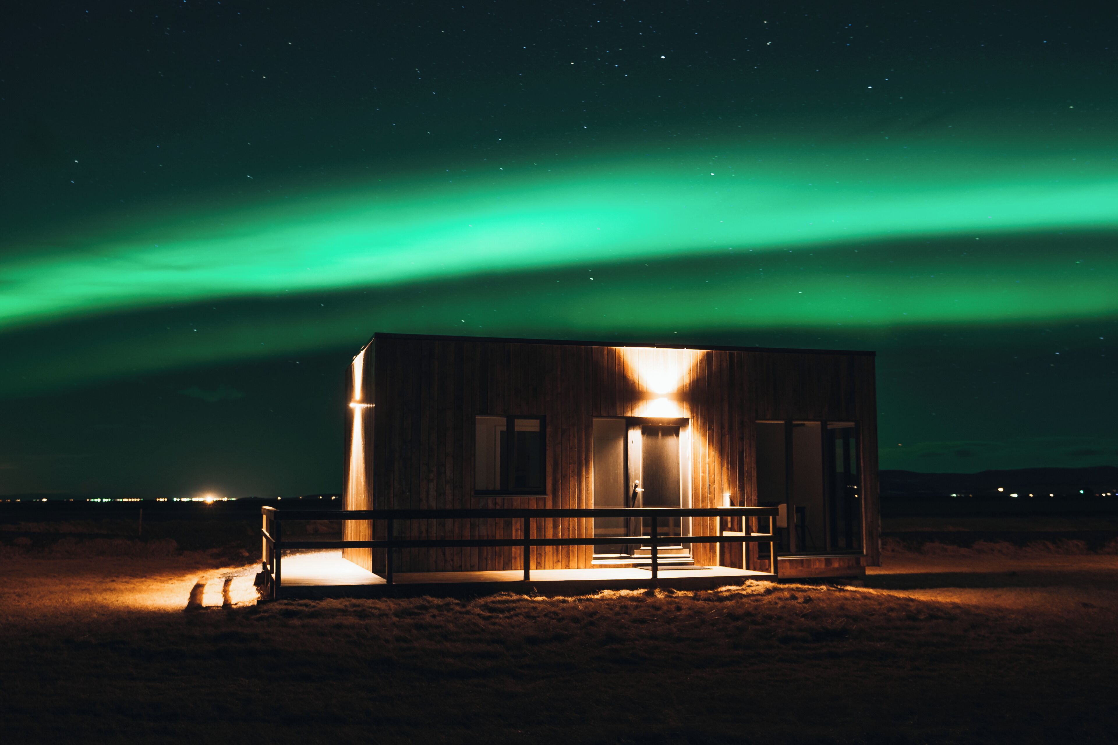 Uma cabana de madeira com varanda, sob um céu noturno com luzes esverdeadas da aurora.