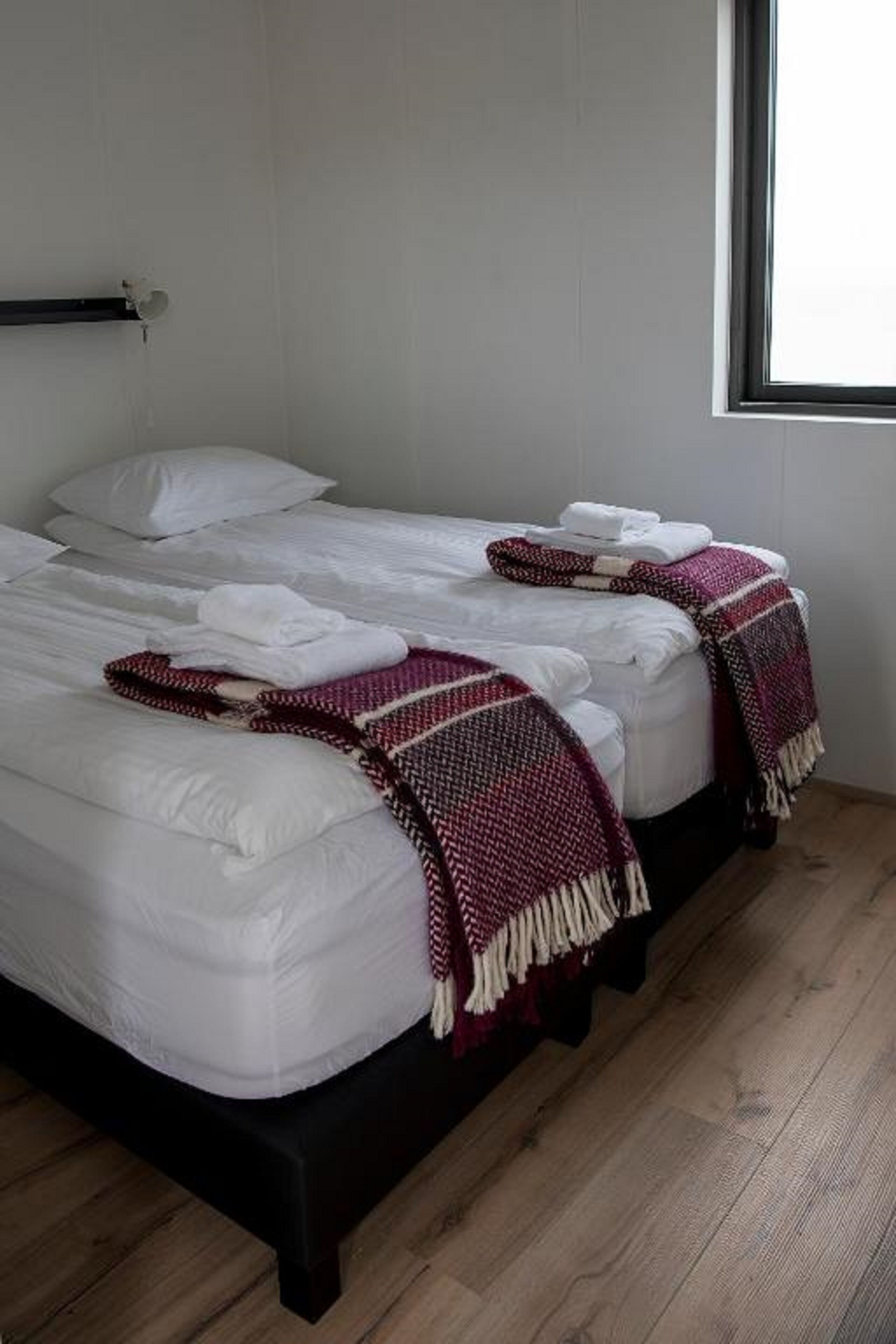 Uma cama de casal com lençóis brancos e duas mantas decorativas em vermelho e branco.
