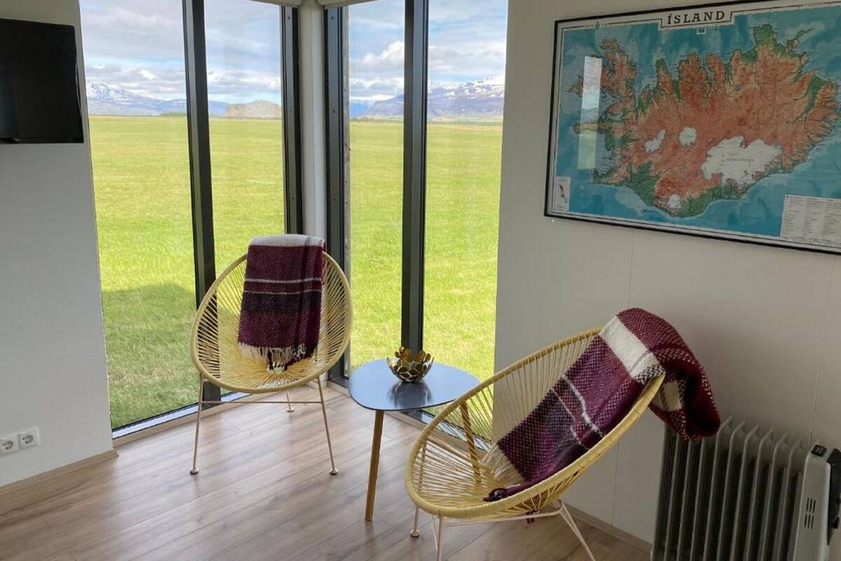 A room with large windows, a map on the wall, and two wicker chairs with blankets.