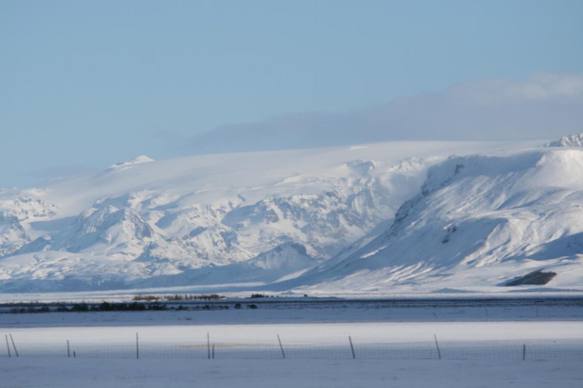 A snow-covered mountain range with a flat, snow-covered plain in the foreground.