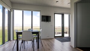 Un área de comedor moderna con una mesa, sillas, ventanas amplias y un televisor de pantalla plana montado en la pared.