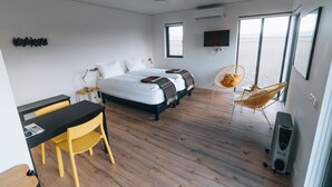 Un dormitorio moderno con cama, escritorio, silla y un amplio ventanal con vistas al mar.