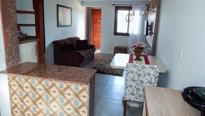 Un espacio habitable compacto con área de cocina, una mesa de comedor, un sofá y una pequeña mesa con un jarrón.