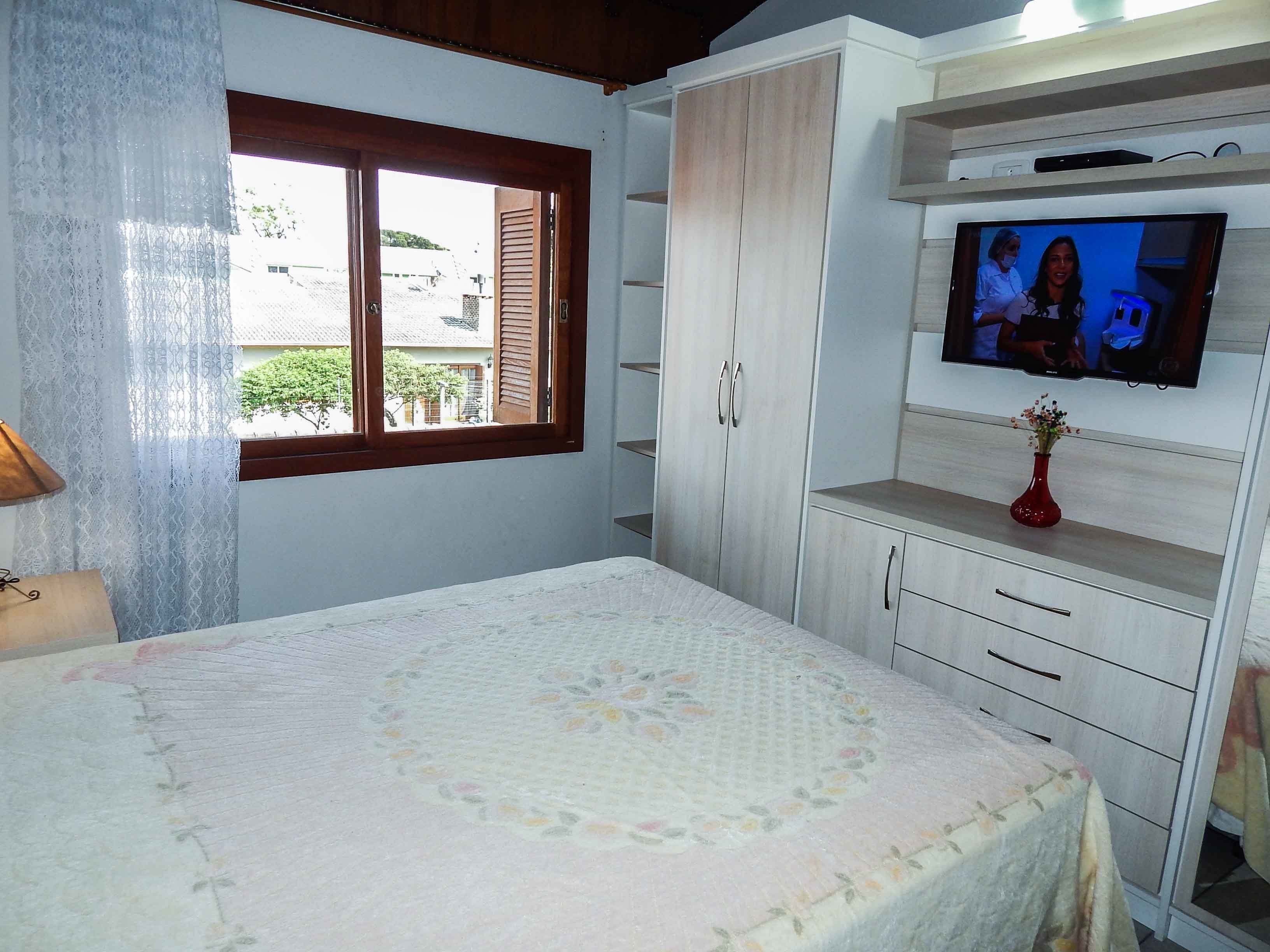 Ein Schlafzimmer mit einem Bett, einem an der Wand montierten Fernseher und einem Fenster mit Vorhängen.