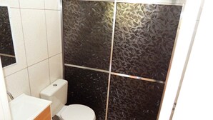 Un baño con inodoro blanco, lavamanos y cabina de ducha con un diseño de hojas en la pared.