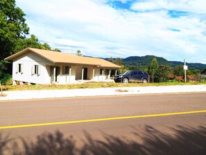A single-story house with a beige roof and white walls, parked in front of a paved road.