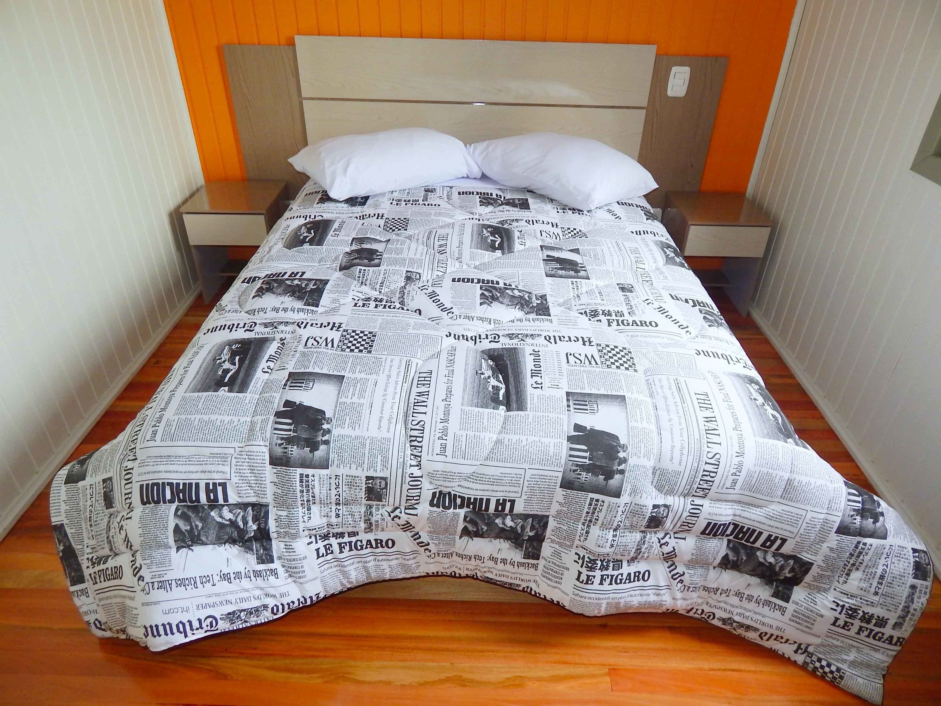 A bed with a newspaper print bedspread, two pillows, and a wooden headboard.