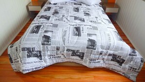 A bed with a newspaper print bedspread, two pillows, and a wooden headboard. - Chales da Serra Gaucha 02 (Gramado)