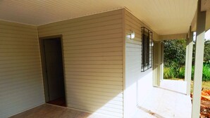 A covered outdoor area with a tiled floor, a door leading inside, and a view of greenery outside. - Chales da Serra Gaucha 02 (Gramado)