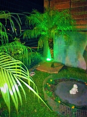 A fenced garden area with a small pond, a palm tree, and a white statue. - Apartamentos Gramado House (Gramado)