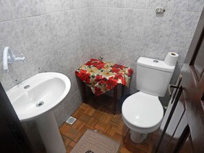 A small bathroom with a sink, toilet, and a small table with a floral tablecloth. - Apartamentos Gramado House (Gramado)