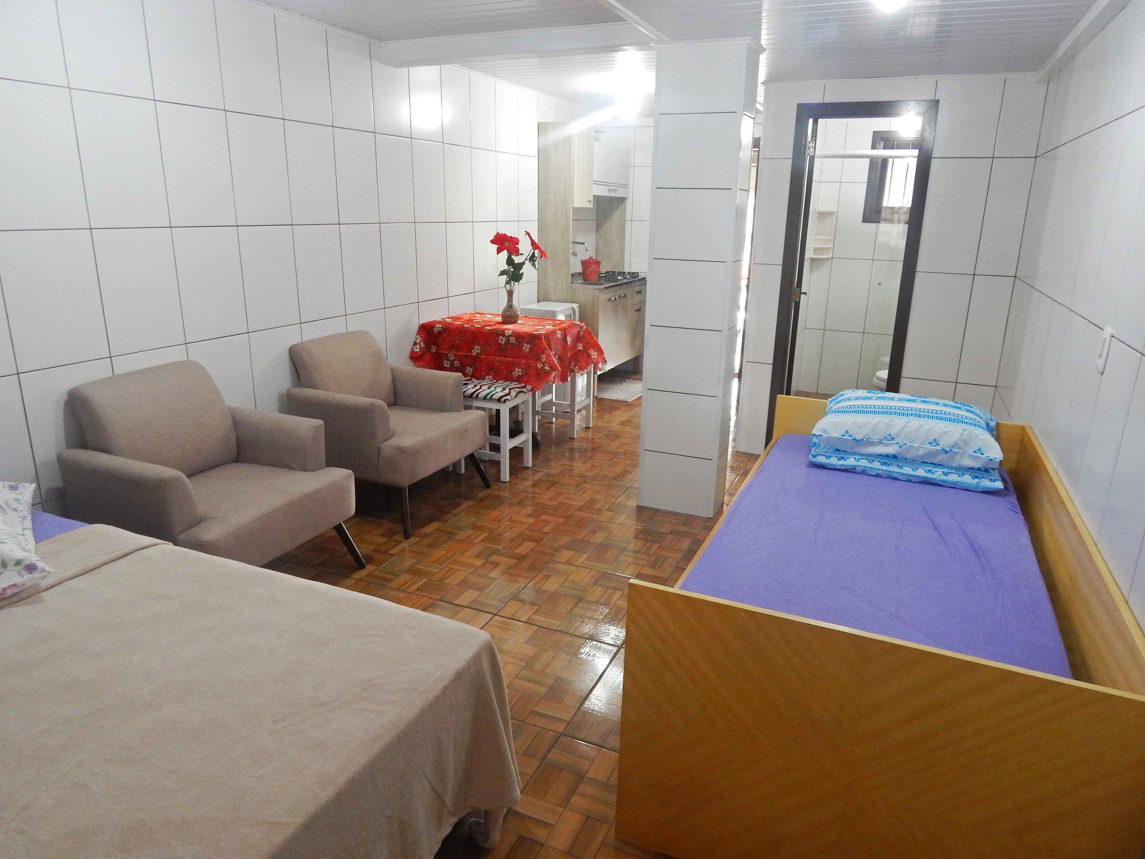 Una habitación compacta con una cama, dos sillas, una mesita con mantel rojo y un espejo.