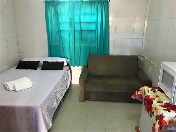 A small, clean room with a bed, a sofa, and a television. - Apartamentos Gramado House (Gramado)