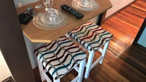 A dining area with a wooden table set for two, two white chairs with patterned cushions, and a remote control on the table. - Residenciais Gramado House (Gramado)