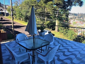 A patio with a glass table and white chairs, a potted plant, and a view of a residential area.