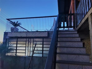 A staircase leading to a balcony with a metal railing, a potted plant, and a view of a body of water.