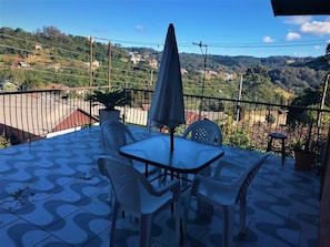 A terrace with a table and chairs, an umbrella, and a view of a hilly landscape.