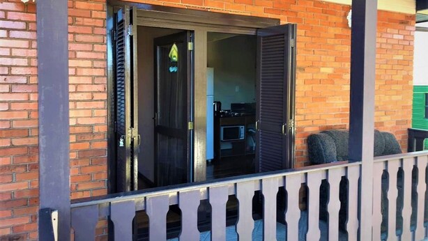 A brick building with a balcony and a door leading to a room with a microwave and a small table. - Residenciais Gramado House (Gramado)