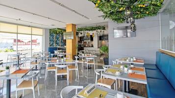 Un restaurante moderno con mesas y sillas blancas, una banqueta azul y plantas colgando del techo.
