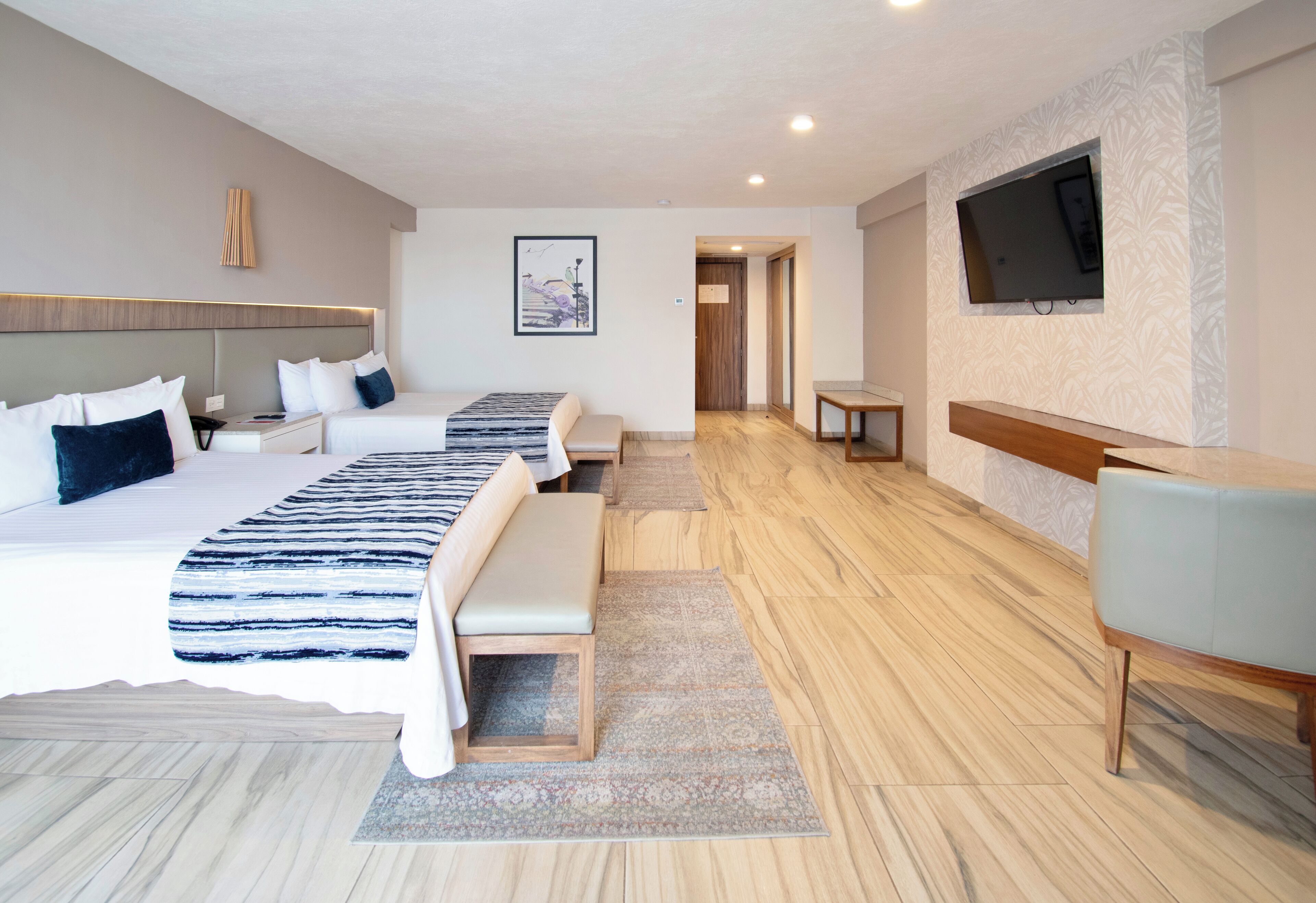 Habitación de hotel con dos camas, un escritorio, un televisor y un baño visible a través de una puerta abierta.