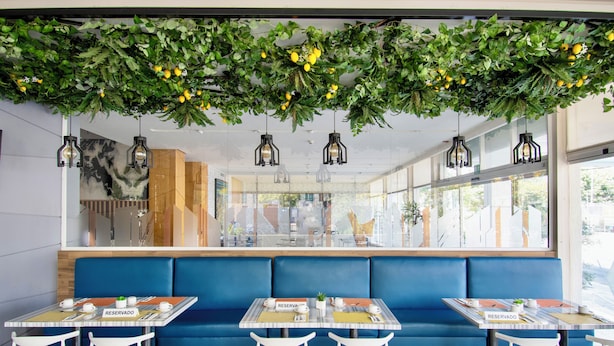 A restaurant with blue booths, tables with 'RESERVADO' signs, hanging lights, and a view through a large window. - Hotel Velvet Plaza (Guadalajara)
