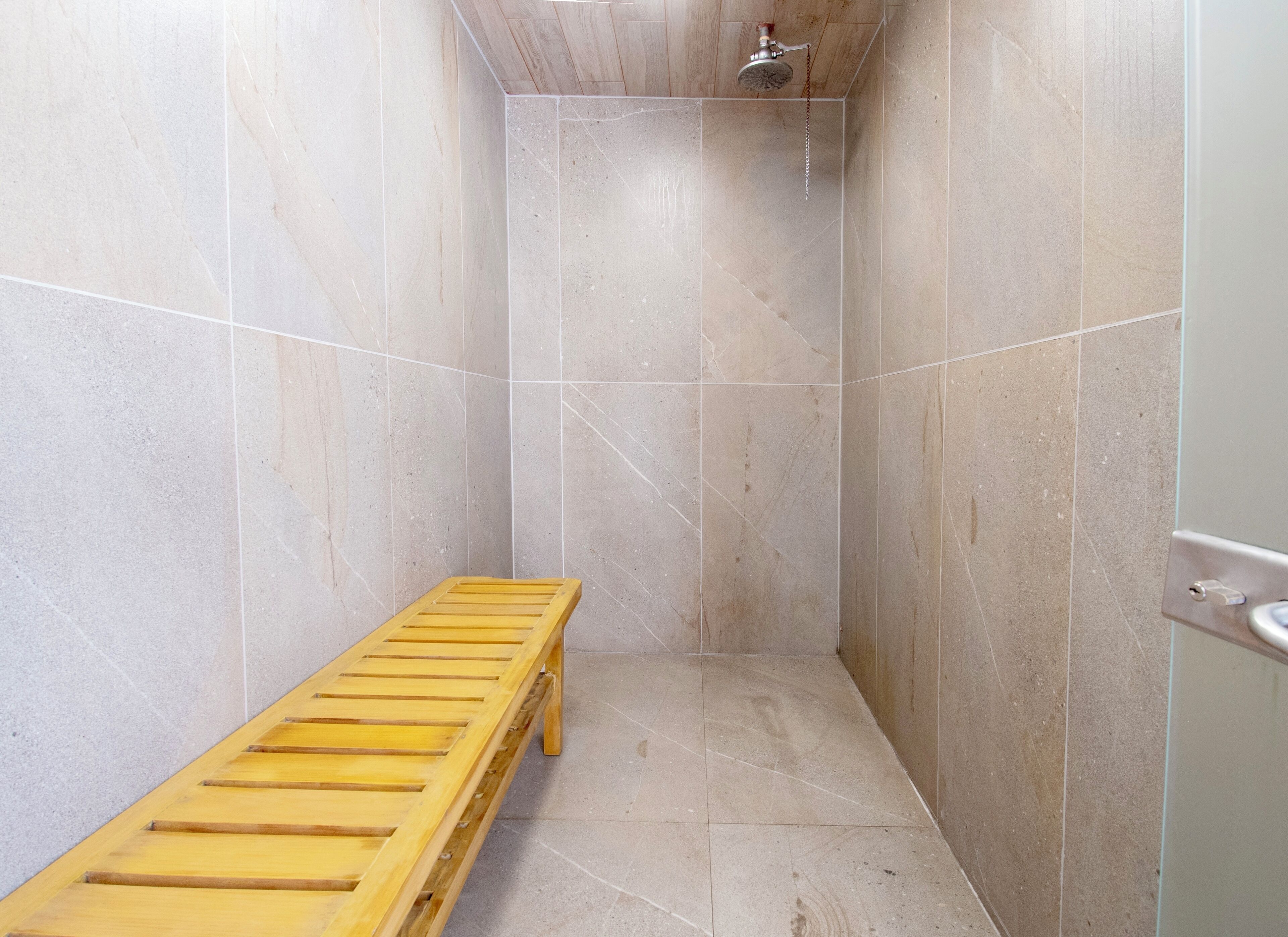 Een douche met een houten bankje, betegelde wanden en een douchekop.