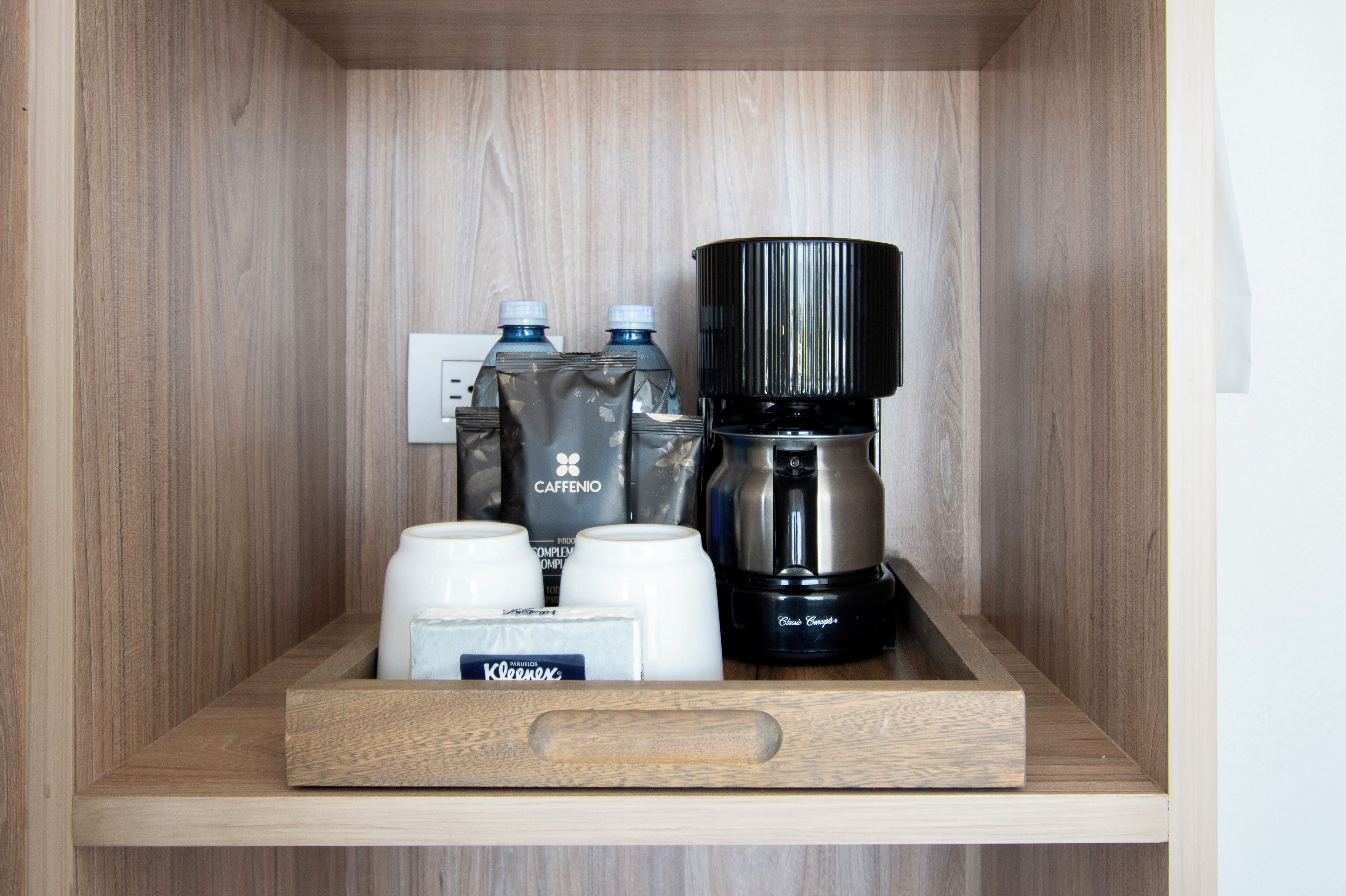 Una repisa de madera con una cafetera, dos botellas de agua y dos tazas blancas.