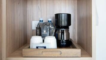 Une étagère en bois avec une machine à café, deux bouteilles d’eau et deux tasses blanches.