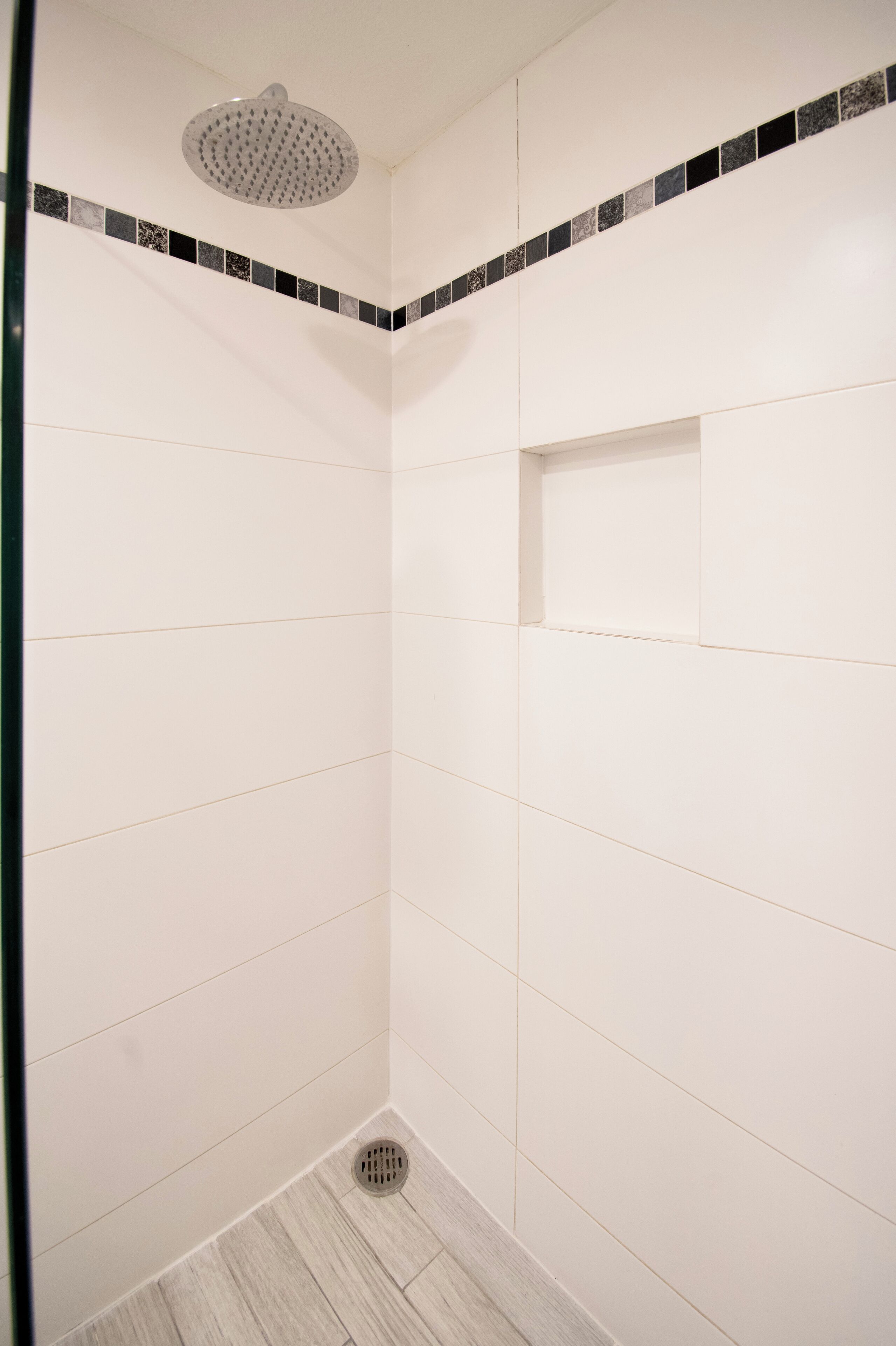 Eine Dusche mit weißen Fliesen und einer schwarz-weißen Bordüre.