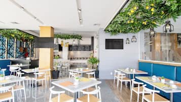 Ein modernes Restaurant mit weißen Tischen, Holzstühlen und hängenden Grünpflanzen an der Decke.