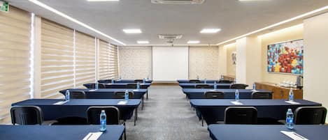 Un salón de conferencias con mesas, sillas y botellas de agua.