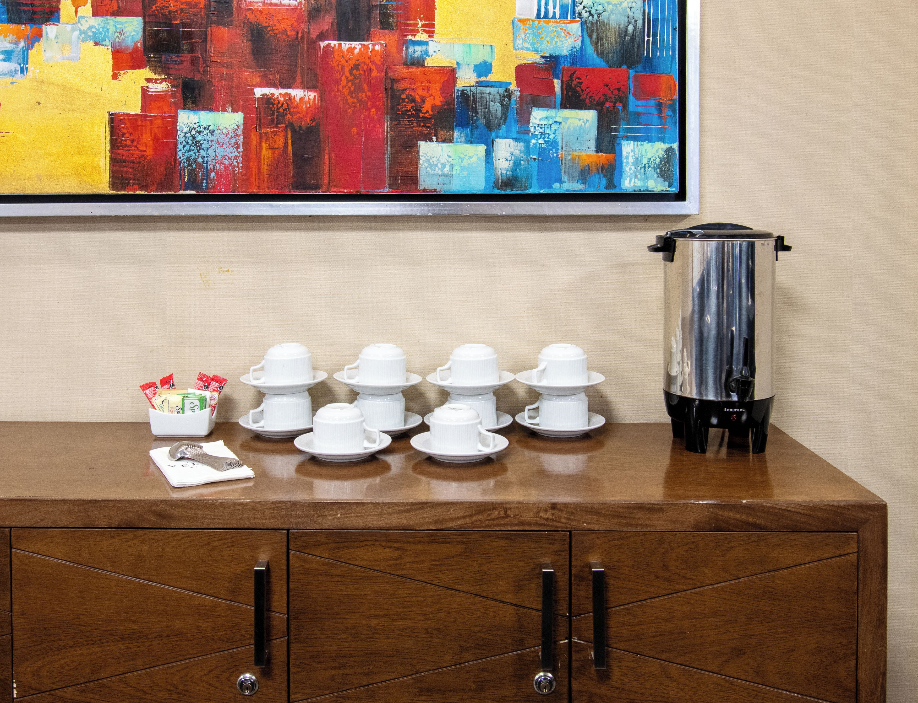 Une table de buffet bien organisée, avec des théières et des tasses blanches, une cafetière et un bol rempli de collations.