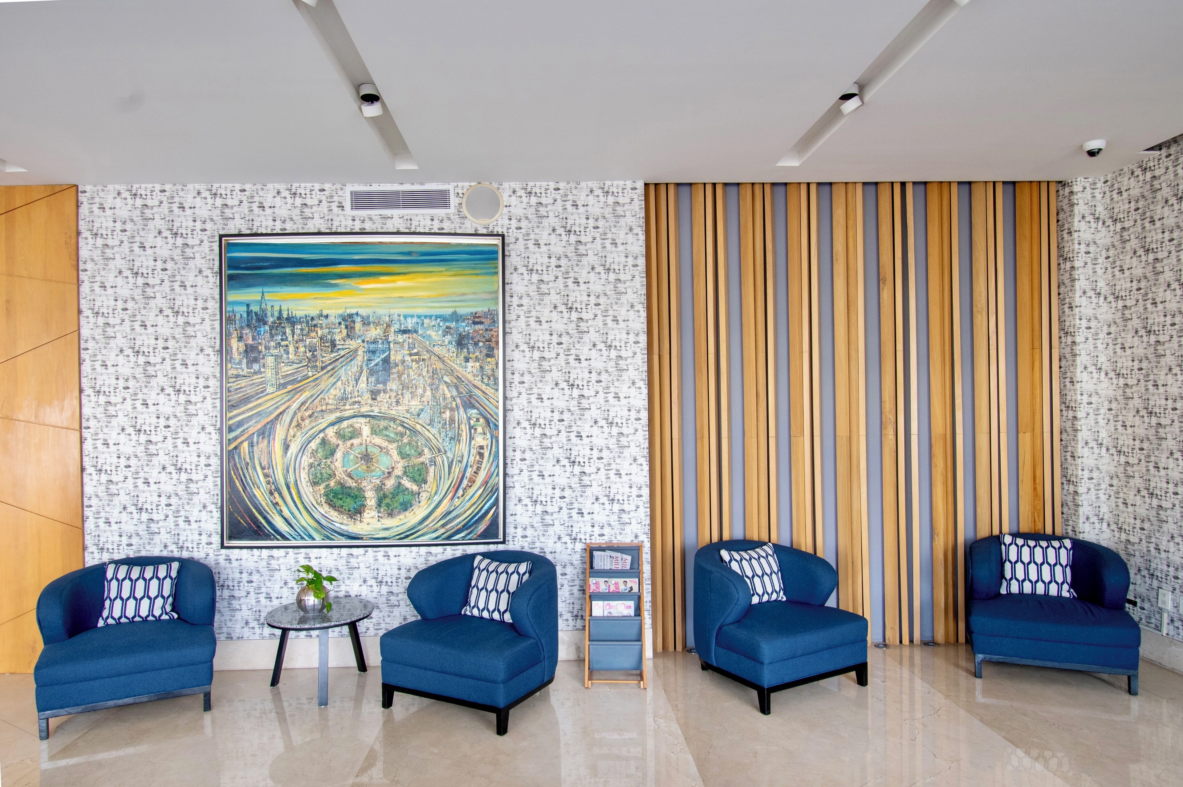A modern lobby with four blue armchairs, a large abstract painting, and a striped wall.