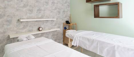 Una habitación con dos camas, una silla de madera, un estante con un reloj y dos espejos colgados en la pared.