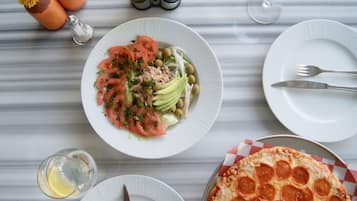 A table with plates of food, a pepper shaker, salt and pepper shakers, a glass of water, and a pizza.
